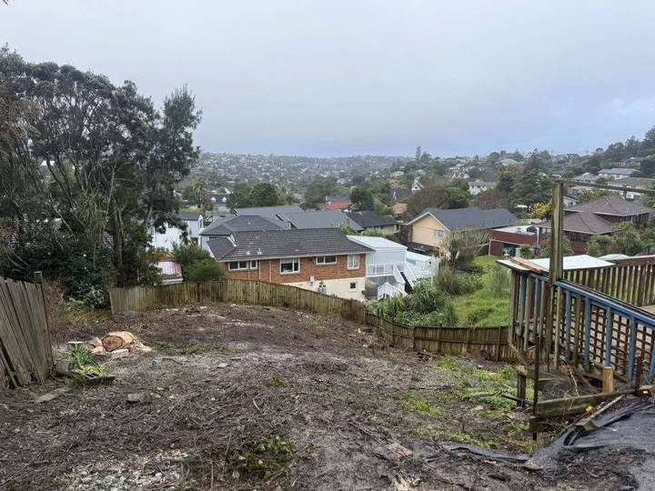 After clearing: the same back section cut back to bare ground with a view over the suburb, a few rounds left by the fence