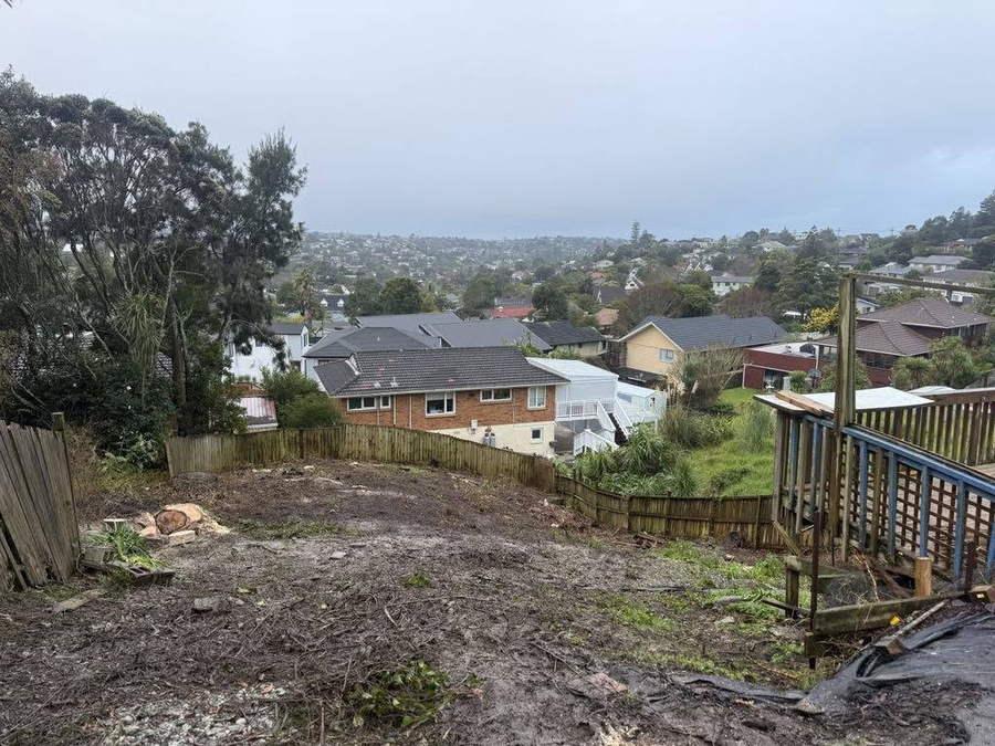 After clearing: the same back section cut back to bare ground with a view over the suburb, a few rounds left by the fence