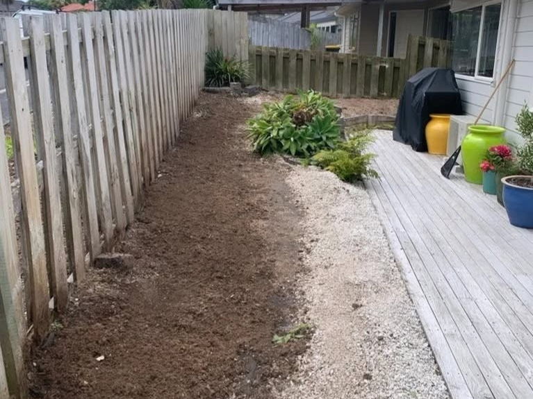 After: the same fence line with the stumps gone and the ground raked level beside the deck
