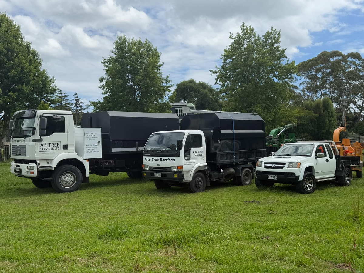 A To Tree Services tipper trucks, a white ute and a trailer chipper lined up on a grass field